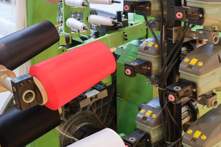 Three red black and white spools of thread are on a machine