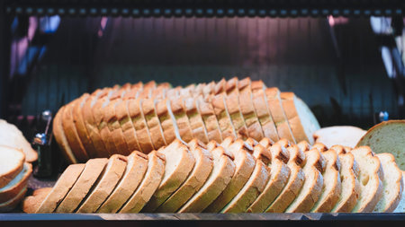 A row of bread loaves are on a conveyor belt, with one loaf missing a piece