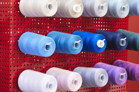 A rack of colorful spools of thread is hanging on a red wall. The spools are of various colors and...