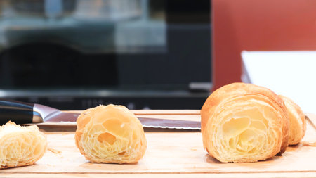Three croissants are on a wooden cutting board. One of them has been cut in halfの写真素材