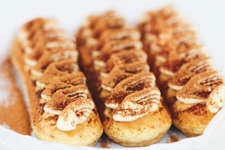 Three brown pastries with white frosting and sprinkles. The pastries are arranged in a row on a white plateの写真素材
