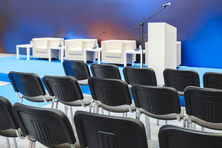 A large auditorium with rows of black chairs and a podium. The chairs are empty and the room is mostly blueの写真素材