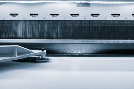 A machine is weaving a fabric with many different colored threads. The machine is blue and whiteの写真素材