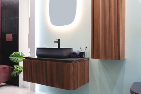 A bathroom with a sink, toilet, and a mirror. The sink is made of wood and has a black faucetの写真素材