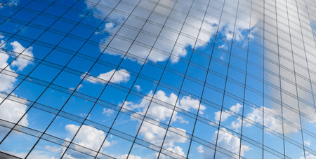 Reflection of a blue sky with white clouds on the glass wall of a skyscraper in the business center...