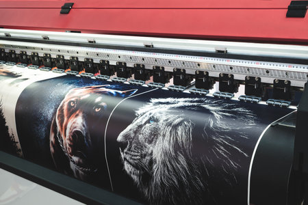 A large printer is printing a series of images, including a dog and a lion. The printer is black and red, and the images are colorful and detailed. The dog is looking at the camera. modern technology concept backgroundの写真素材