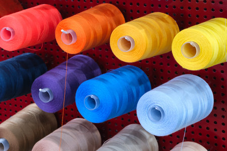 A row of colorful spools of thread hanging on a red wall. The spools are of different colors and...