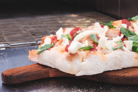 A pizza with a lot of toppings including cheese, spinach, and tomatoes. The pizza is on a wooden cutting boardの写真素材