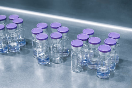 A row of purple and clear bottles with purple lids. The bottles are lined up on a table, pharmaceutical production of drugs and vaccinesの写真素材