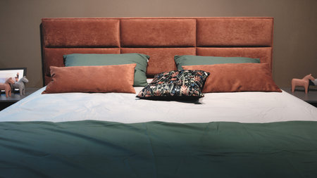 A bed with a headboard and pillows. The headboard is pink and the pillows are blue and green