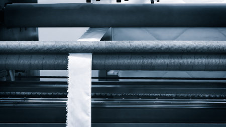 A roll of white fabric is being cut by a machine. The machine is cutting the fabric into strips