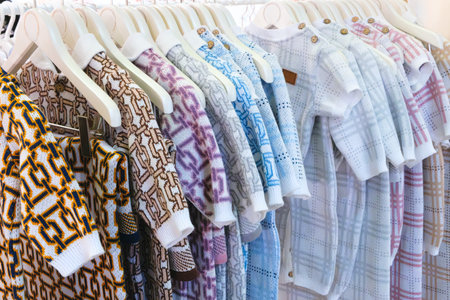 Rack of baby clothes with a variety of colors and patterns. The clothes are hanging on a white rackの写真素材