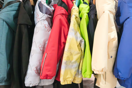 A row of colorful jackets hanging on a rack. The jackets are of different colors and styles, including red, yellow, green, and blue. The jackets are neatly arrangedの写真素材