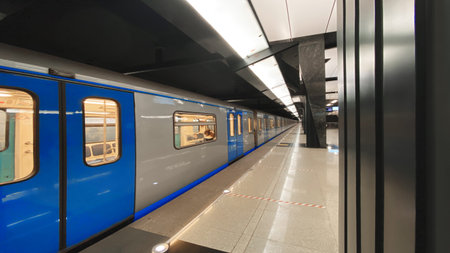 A blue and silver train is parked at a station. The train is long and has a blue door