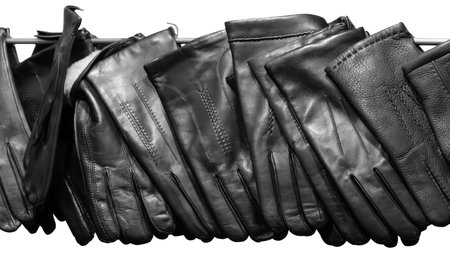 A row of black leather gloves are lined up on a shelf. The gloves are all the same size and shape, and they are all black. The gloves are arranged in a neat and orderly fashionの写真素材