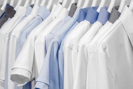 A row of white and blue shirts hanging on a clothesline. The blue shirt is the only one with a patternの写真素材