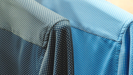 Two blue and black shirts with a pattern of dots. The shirts are folded and placed on a chair