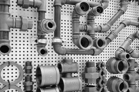 wall of pipes and fittings made of black, white and shiny metal. Concept of industrial and mechanical background of water supply and sewerageの写真素材