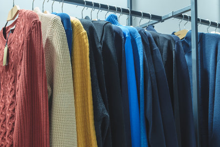 A rack of clothes with a blue sweater on top. There are many different colors and styles of clothing, including a red sweater, a yellow sweater, and a black sweater. The clothes are neatly hung upの写真素材