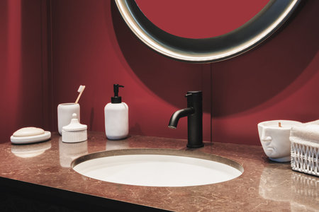 A red bathroom interior sink with black faucet mirror candle and a bottle of perfume on the counter.