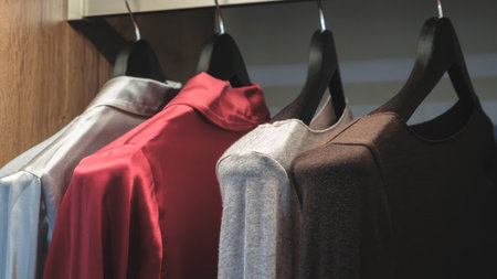 A row of clothes hanging on a rack, including a red shirt, a gray shirt, and a brown shirtの写真素材