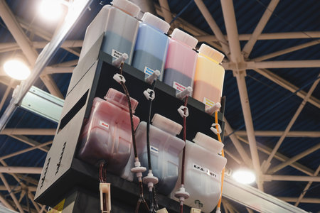 A row of multi-colored ink bottles for an industrial printer. The bottles are labeled with different...