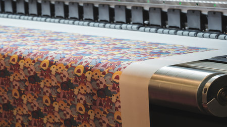 A machine is printing a colorful piece of fabric with a pattern of animals. The machine is in a factory settingの写真素材