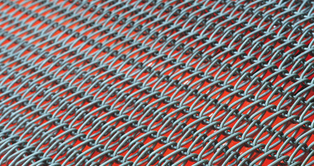 A close up of a chain link fence with a red background. The fence is made of metal and has a lot of...