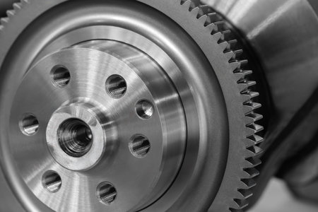 A close up of a gear with many holes. The gear is silver and has a black rim industrial concept...