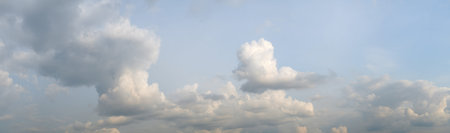 A wide panorama of the sky with clouds. The clouds are white and fluffy, and they are scattered all...