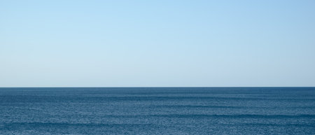 ocean is calm and clear, with no visible waves or ripples. the sky is a bright blue, and the sun is shining brightly. scene is peaceful and serene, with sense of calm and tranquilityの写真素材