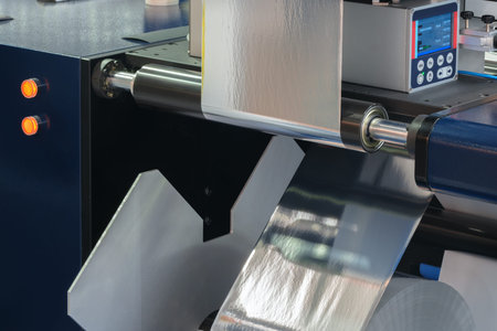 Roll of plastic film is being made in a factory. The roll is being fed into a machine that is...