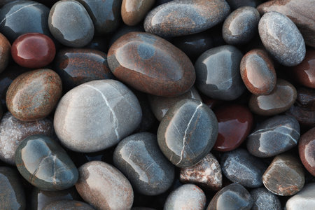Pebbles round wet smooth colorful stones on sea beach illuminated by morning sun as texture spa...