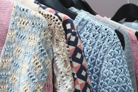 A row of knitted sweaters hang on a rack. The sweaters are of different colors and patterns,...