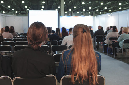 Women sit in a room with a projection screen in a conference room and listen to and watch a business...