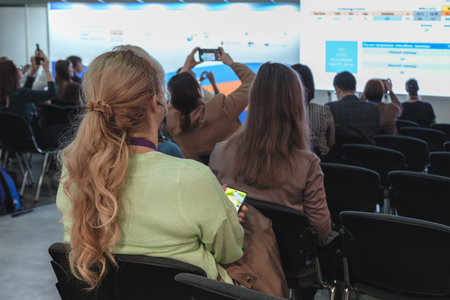 Women sit in a room with a projection screen in a conference room and listen to and watch a business...