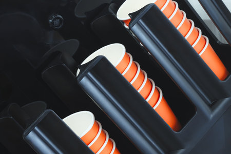 A black container near a coffee bar with orange cups inside for coffee sales. The cups are lined up.