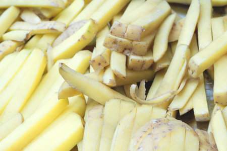 A pile of yellow potatoes cut for French fries. The potatoes lie on a cutting board.
