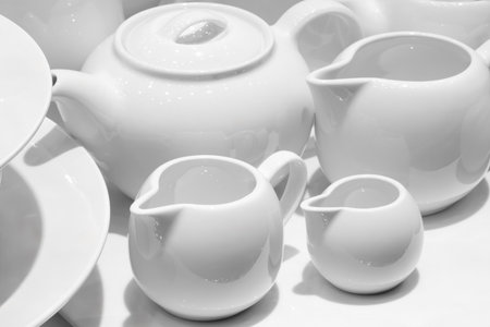 A collection of white dishes, including cups, bowls, and a teapot, are piled on top of each other.の写真素材