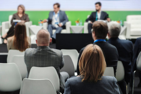 Audience is attentive to panel discussion. Speakers sit confidently on elevated stage. Participants...