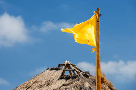 Yellow flag against the background of thached roof and blue skyの写真素材