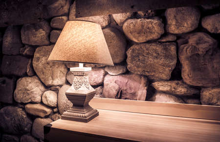Stone wall illuminated by stylish lamp on wooden tableの写真素材