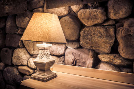 Stone wall illuminated by stylish lamp on wooden tableの写真素材