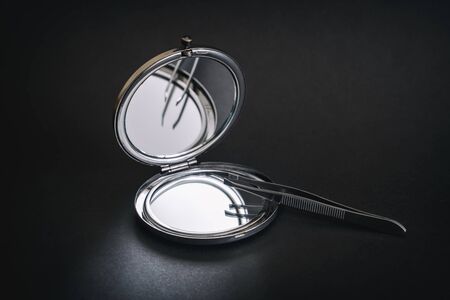 Foldable Pocket Mirror And Tweezers On A Dark Surfaceの写真素材