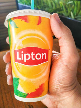 Hand holding a cardboard soft drink cup with Lipton logo. Lipton, a British tea brand, ready-to-drink beverages are sold by Pepsi Lipton International.のeditorial素材