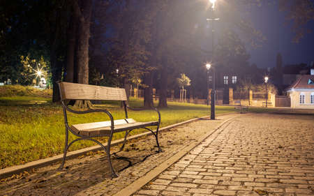 Wooden Bench in a City Park Illuminated by a Street Lamp, Inviting Night Calm Moodの写真素材