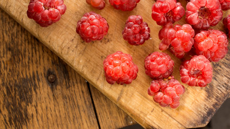 Red Raspberry on wooden chopping board and table. High resolution image presenting several red...