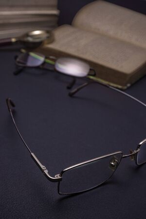 Books with glasses on black table and wooden background. High resolution image depicting reading/bokks industry.の写真素材