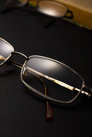 Books with glasses on black table and wooden background. High resolution image depicting reading/bokks industry.の写真素材