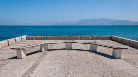 Empty stone bench on the Greek coast on juicy blue clear sky and sea. Summer feeling. Empty space, minimalism concept, no people.の写真素材